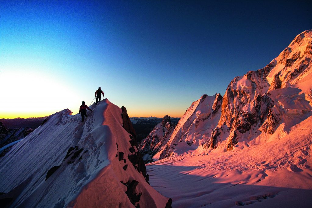 Alba sulla Cresta Kuffner al Mont Maudit (4465 m), una grande classica del Gruppo del Monte Bianco. Sulla destra il Ghiacciaio della Brenva, oltre il quale si alzano l’Aiguille Noire de Peutérey (3773 m), le Aiguilles Blanches de Peutérey (4114 m e 4108 m) e il Grand Pilier d’Angle (4243 m). Foto @ Mario Colonel