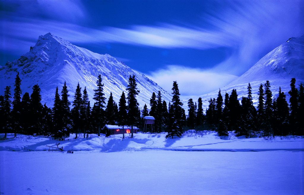 La baita nel cuore dell'inverno. Un caldo focolare attorniato dal gelo luccicante. In cielo un accenno di aurora. Foto 1973-1999 Richard Proenneke