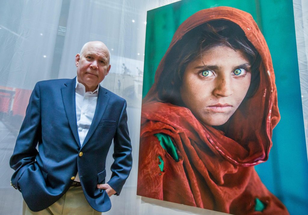 Steve McCurry in posa accanto a uno dei suoi scatti più celebri: