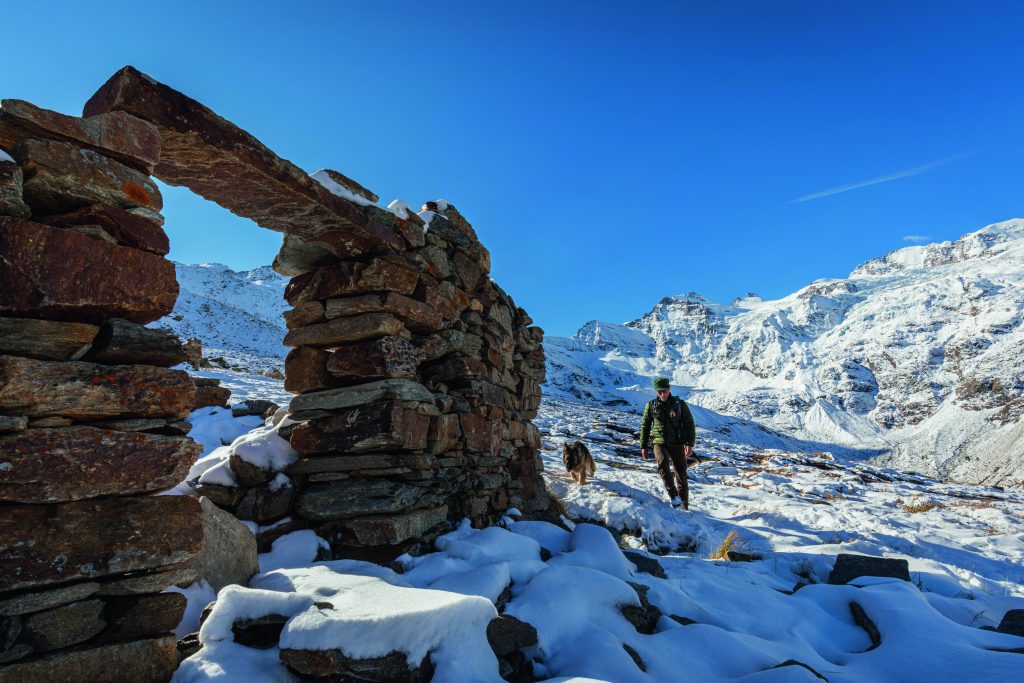 Un guardaparco con
il suo cane, ai casolari
di Money. Sullo sfondo,
la Testa di Valnontey
e quella della Tribolazione, la Punta di Ceresole
e, all’estrema destra,
il Gran Paradiso. Foto di Stefano Torrione
