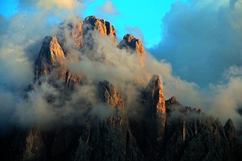 Le ultime nebbie della sera si diradano, scoprendo la vetta del Sassolungo (3181 m). La parete nord, che precipita sulla Val Gardena, offre una delle più belle visioni delle Dolomiti. Foto Umberto Isman