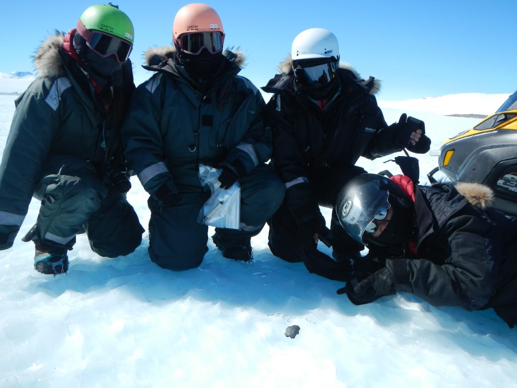 Il team di ricerca in posa davanti a un meteorite nella "blue ice zone" del ghiacciaio Nils Larsen (da sinistra a destra: Maria Valdes, Vinciane Debaille, Maria Schönbächler, Ryoga Maeda) ©Vinciane Debaille