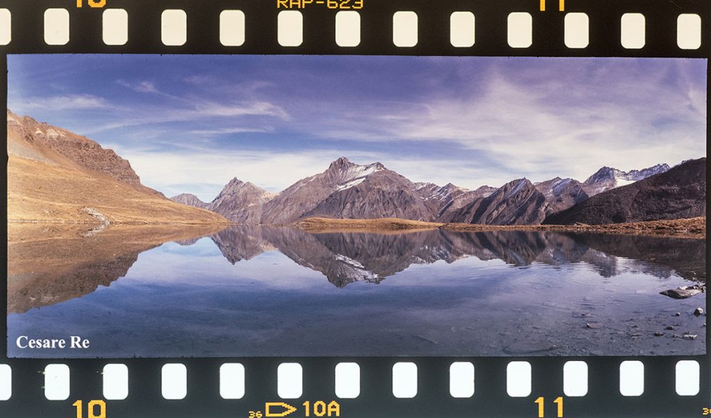 Il Lago Djouan, in Valsavarenche, con la Grivola che si specchia. Scattata con la fotocamera a pellicola Horizon 202, ad obiettivo rotante, senza esposimetro, con una meccanica “avventurosa”, ma ottica di buona qualità. Il fotogramma è di dimensioni 24 per 58 mm. Pellicola diapositiva. Il bordino che si vede non è aggiunto in post produzione, ma è quello originale che consente l’aggancio della pellicola al rocchetto. Sì lo so, cose da dinosauri, per alcuni, un bel ricordo per molti fotografi. Poi, infondo, qualcuno usa ancora la pellicola. Io, ogni tanto, qualche rullino lo scatto.