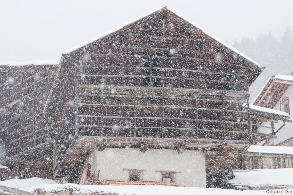 Nevica in Val Gardena. L’eccezione che conferma la regola. Per rendere evidente i fiocchi di neve è meglio cercare uno sfondo scuro, come la casa tipica, in questa situazione. Il tempo di posa, però, non deve essere lento, altrimenti i fiocchi scomparirebbero. Nikon D300; Nikkor 24-120 afd 3,5 / 4,5. 1/250 di secondo (eh sì, molto veloce); f 5; iso 200.