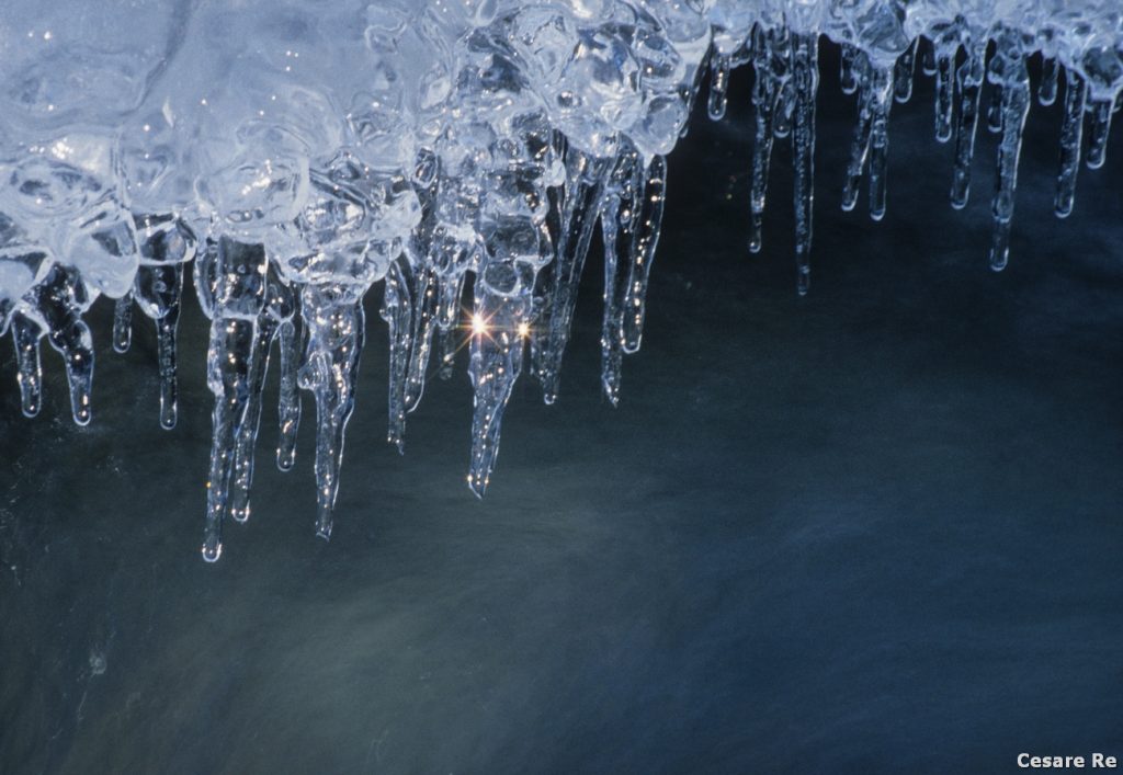 Piccole stalattiti di ghiaccio, nel greto di un torrente. Nikon F90X; Nikkor 80-200 2,8 AFD; Fujichrome Velvia 50. Treppiede. Il tempo di posa lungo è stato opportuno per rendere il mosso dell’acqua che scorre sotto al soggetto. 