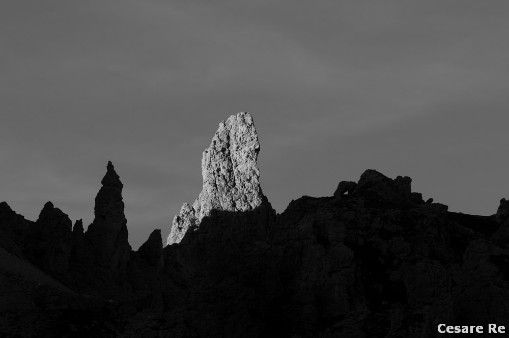 Cielo libero, sgombro da nubi. Da questa foto, nasce l’idea del mio progetto fotografico “Linee e Forme, Luci e Ombre “, dove cime dolomitiche, o parti di cime dolomitiche emergono dalle ombre verso la luce. Ero al Passo Gardena a fotografare il tramonto. Questo attimo è stato l’inizio di un’idea. Il pinnacolo che si erge dalle ombre si trova al Passo Cir, uno dei luoghi più suggestivi del Parco Puez Odle. A volte il progetto fotografico, una serie di immagini legate le une alle altre da criteri concettuali o estetici o di comunicazione, nasce in maniera ragionata e ponderata. In alti casi, come in questo, è una singola situazione a suggerire un’idea che andrà poi sviluppata e approfondita. La misurazione dell’esposizione è stata effettuata in modalità spot, sulle parti luminose, con sottoesposizione per accentuare già in ripresa l’ombra scura. 